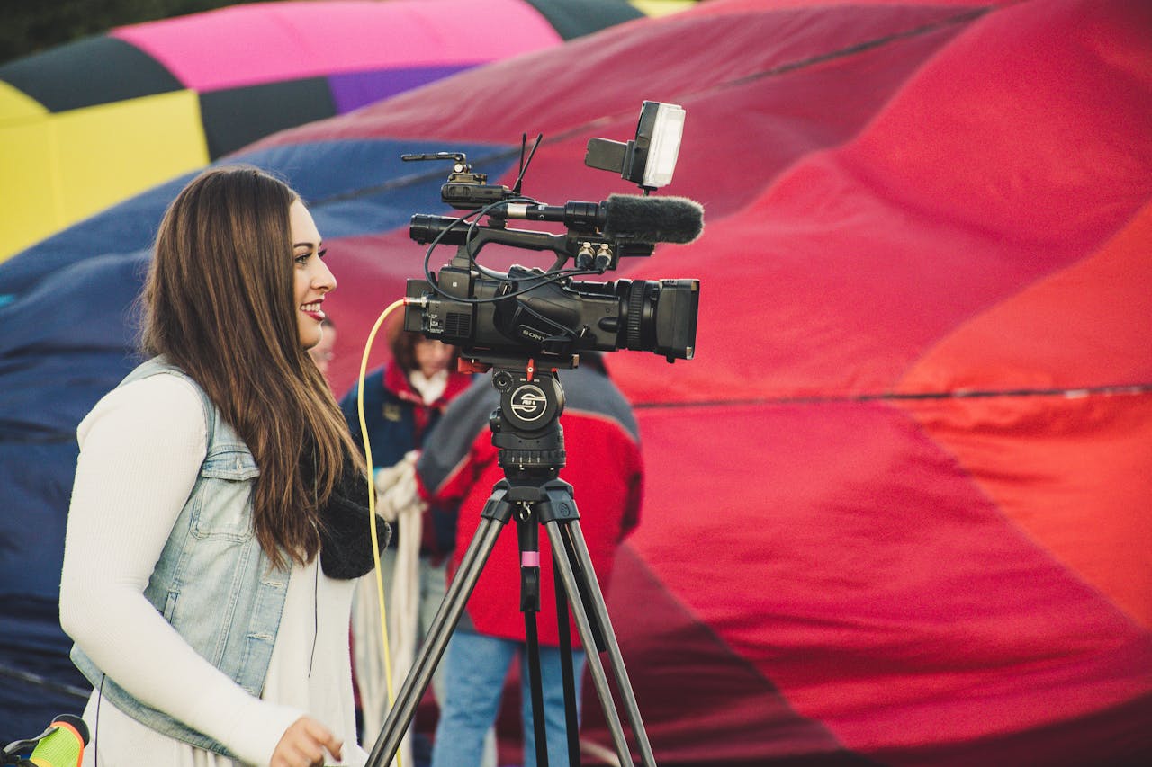 home-hero A female videographer operates a camera before a colorful hot air balloon backdrop.