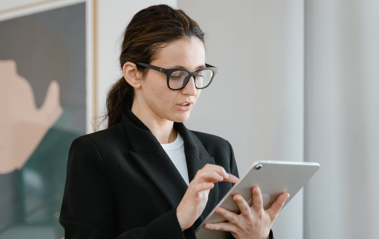 Caucasian woman in office attire using a tablet indoors with a blurred background.